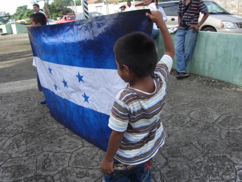 Kinder halten die Fahne von Honduras vor den Installationen der Migrationspolizei hoch. Die große Mehrheit jugendlicher und erwachsener Migranten kommt aus dem mittelamerikanischen Land, das unter den Folgen des Putsches im Jahr 2009 leidet