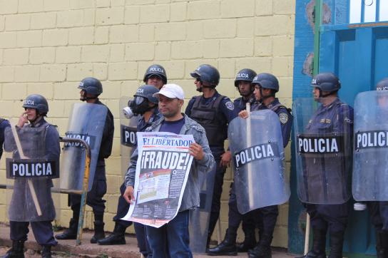 Demonstrant hält in Honduras vor Polizisten eine Zeitung
